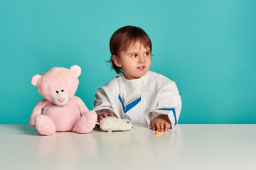 Smiling little girl in medical uniform play with stethoscope and teddy bear. Studio shot
