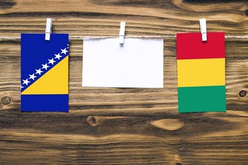 Hanging flags of Bosnia Herzegovina and Guinea attached to rope with clothes pins with copy space on white note paper on wooden background.Diplomatic relations between countries.