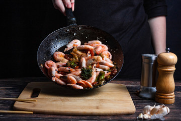 Chef at work. Hand holds a hot pan with fried shrimp and vegetables in sweet and sour sauce.