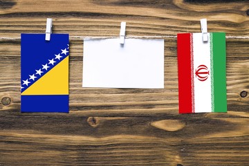 Hanging flags of Bosnia Herzegovina and Iran attached to rope with clothes pins with copy space on...