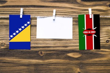 Hanging flags of Bosnia Herzegovina and Kenya attached to rope with clothes pins with copy space on white note paper on wooden background.Diplomatic relations between countries.