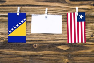 Hanging flags of Bosnia Herzegovina and Liberia attached to rope with clothes pins with copy space on white note paper on wooden background.Diplomatic relations between countries.