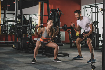 excited trainer shouting while motivating attractive sportswoman lifting barbell