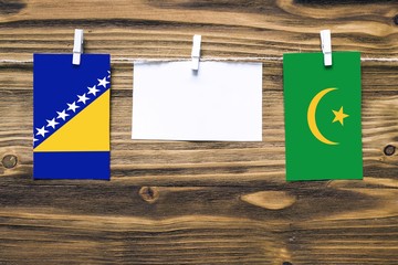 Hanging flags of Bosnia Herzegovina and Mauritania attached to rope with clothes pins with copy space on white note paper on wooden background.Diplomatic relations between countries.