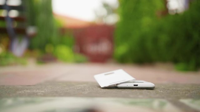 Mobile phone falls and breaks on the concrete ground in slow motion