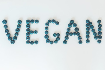 The word Vegan made of fresh blueberries. Healthy food fruit lettering on white background. Organic and vegan meal concept
