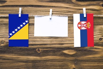 Hanging flags of Bosnia Herzegovina and Serbia attached to rope with clothes pins with copy space on white note paper on wooden background.Diplomatic relations between countries.