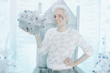 christmas blonde caucasian guy in white sweater with stars holding and opening gift present on the chair