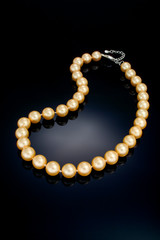 A single strand golden color pearl necklace sits on a black refective background.