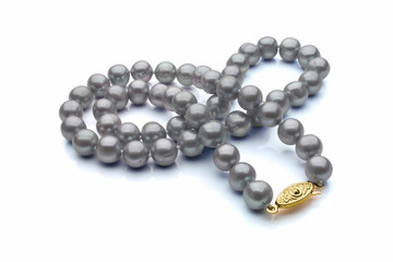 A single strand necklace of grey pearls with a gold clasp are crossed over itself. Shown on a white background with shadow.
