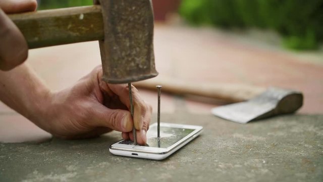 A man hammers a nail into the phone on the concrete ground in slow motion