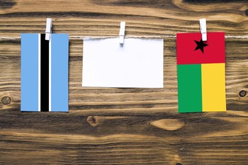 Hanging flags of Botswana and Guinea Bissau attached to rope with clothes pins with copy space on white note paper on wooden background.Diplomatic relations between countries.