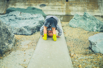 Little toddler with his head between his legs on a rocky beach