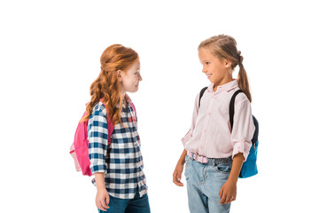 happy schoolkids with backpacks looking at each other isolated on white