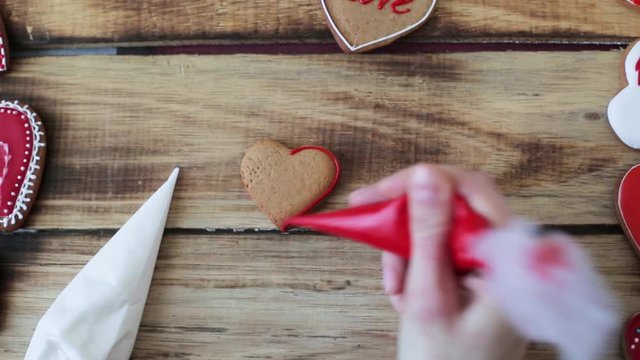 Heart shaped cookies decorating process with pink cream. Closeup of female hand holding a tube of pink cream