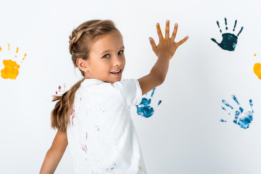 Kid with blue and yellow paint on hands near hand prints on white
