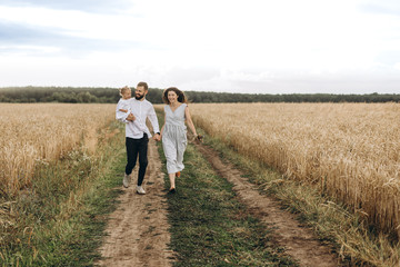 happy family on the walk in the wheat field: Father and a cute young wife with her little daughter happy parents with her baby