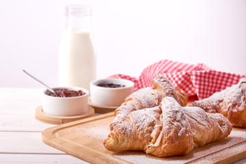 Still life on old wooden board table with three sweet croissants and fruit jam. Glass of milk