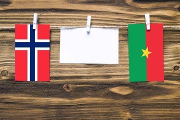 Hanging flags of Bouvet Islands and Burkina Faso attached to rope with clothes pins with copy space on white note paper on wooden background.Diplomatic relations between countries.