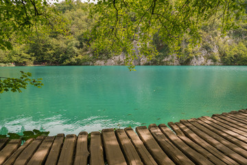 Fototapeta na wymiar Wooden path along the lake under green trees in the Plitvice Lakes park