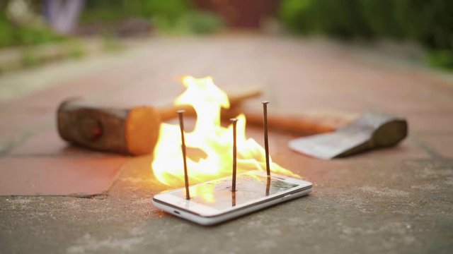 Broken with nails mobile phone on ground is on fire in slow motion