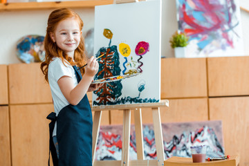 happy redhead kid painting on canvas in art school