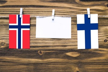 Hanging flags of Bouvet Islands and Finland attached to rope with clothes pins with copy space on white note paper on wooden background.Diplomatic relations between countries.