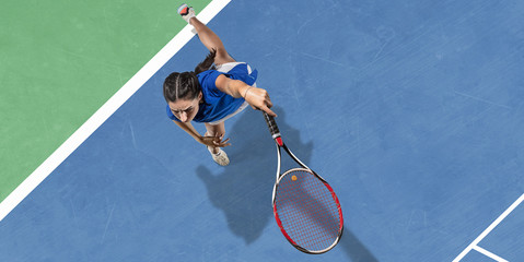 Young caucasian brunette woman in blue shirt playing tennis at the court. Hits ball with racket,...