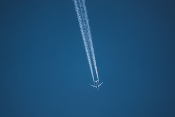 a large passenger aircraft flies in the cloudless blue sky and produces a white glowing condensation trail