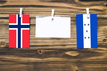 Hanging flags of Bouvet Islands and Honduras attached to rope with clothes pins with copy space on white note paper on wooden background.Diplomatic relations between countries.