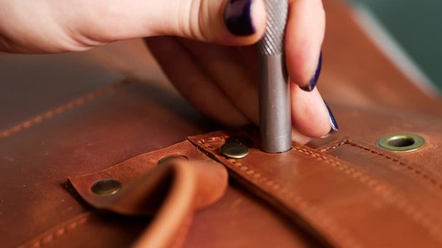 Female worker puts rivets on leather bag straps with chisel and hummer. Crafted handmade manufactures. Close up 4k