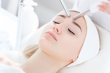 Obraz na płótnie Canvas Beautician makes a microcurrent massage of face of girl client with help of modern salon equipment. The concept of hardware cosmetology. Cosmetic anti-aging procedure in clinic, facial skin care