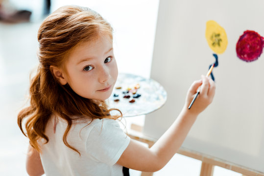 selective focus of cute redhead kid painting in art school