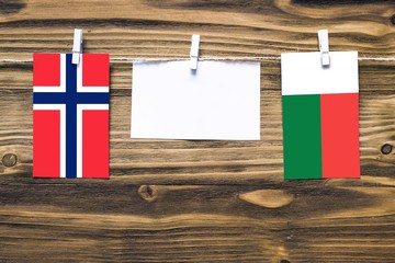 Hanging flags of Bouvet Islands and Madagascar attached to rope with clothes pins with copy space on white note paper on wooden background.Diplomatic relations between countries.