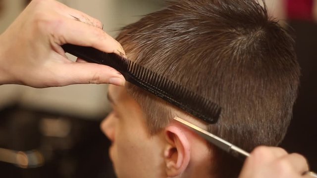 Woman hairdresser scissors boy in salon doing stylish hairstyle. 