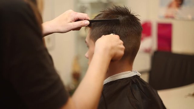 The hairdresser cuts the boy's hair clipper in the salon, making a stylish hairstyle.