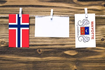 Hanging flags of Bouvet Islands and Mayotte attached to rope with clothes pins with copy space on white note paper on wooden background.Diplomatic relations between countries.