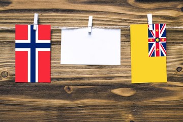 Hanging flags of Bouvet Islands and Niue attached to rope with clothes pins with copy space on white note paper on wooden background.Diplomatic relations between countries.