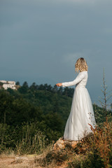 Fototapeta na wymiar Beautiful elegant bride in lace wedding dress with long full skirt and long sleeves. Pretty girl in white. Nature, with city in the background.