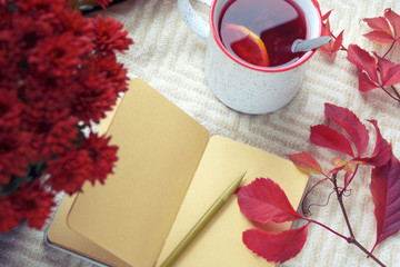 Naklejka na ściany i meble Autumn, fruit tea, red chrysanthemum and a notepad with blank sheets on a warm blanket. Hygge concept. Loneliness and autumn melancholy. Depression.