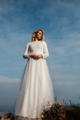 Fototapeta na wymiar Beautiful elegant bride in lace wedding dress with long full skirt and long sleeves. Pretty girl in white. Nature, with city in the background.