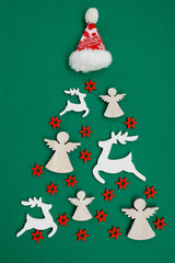Christmas tree made of New year`s wooden decorations and Santa Claus mini hat on green background. Holiday concept. Vertical picture