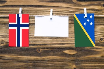 Hanging flags of Bouvet Islands and Solomon Islands attached to rope with clothes pins with copy space on white note paper on wooden background.Diplomatic relations between countries.