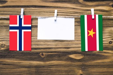 Hanging flags of Bouvet Islands and Suriname attached to rope with clothes pins with copy space on white note paper on wooden background.Diplomatic relations between countries.