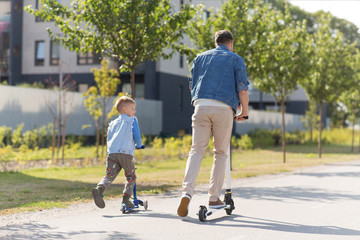 family, leisure and fatherhood concept - happy father spending time with little son riding scooter...