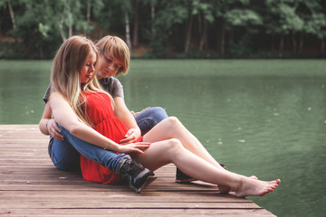 A happy married couple Husband hugs a beautiful adult pregnant wife. walks in a park by the lake. Second trimester. Holds her hands on her stomach. The benefits of walking during pregnancy.