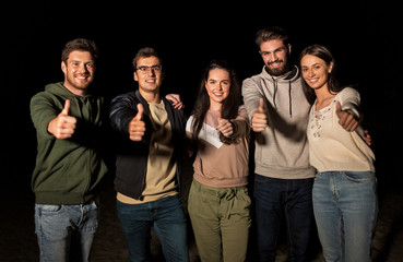 leisure and people concept - group of happy smiling friends showing thumbs up outdoors at night