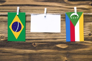 Hanging flags of Brazil and Comoros attached to rope with clothes pins with copy space on white...