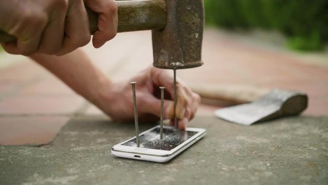 A man hammers a nail into the phone on the concrete ground in slow motion