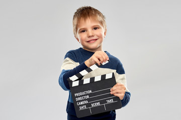 production, filmmaking and cinematography concept - portrait of nice little boy with clapperboard...